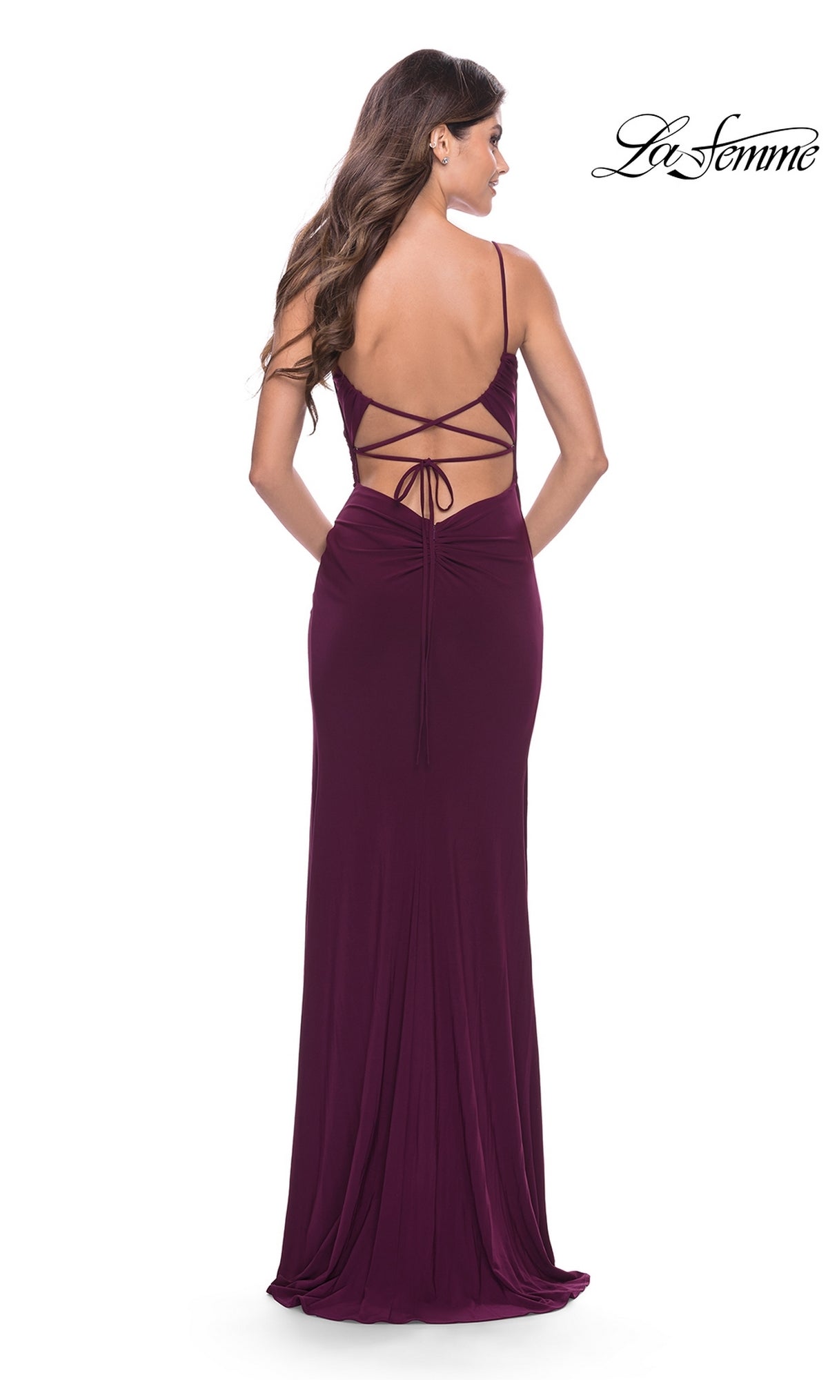 A woman stands with her back to the camera in the Strappy-Back Long La Femme Prom Dress 31078, a floor-length, backless gown featuring crisscrossed straps. La Femme logo appears in the top right corner.